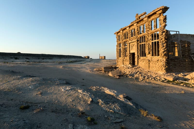 Fassade eines verfallenen zweistöckigen Hauses am Rand einer Sandpiste