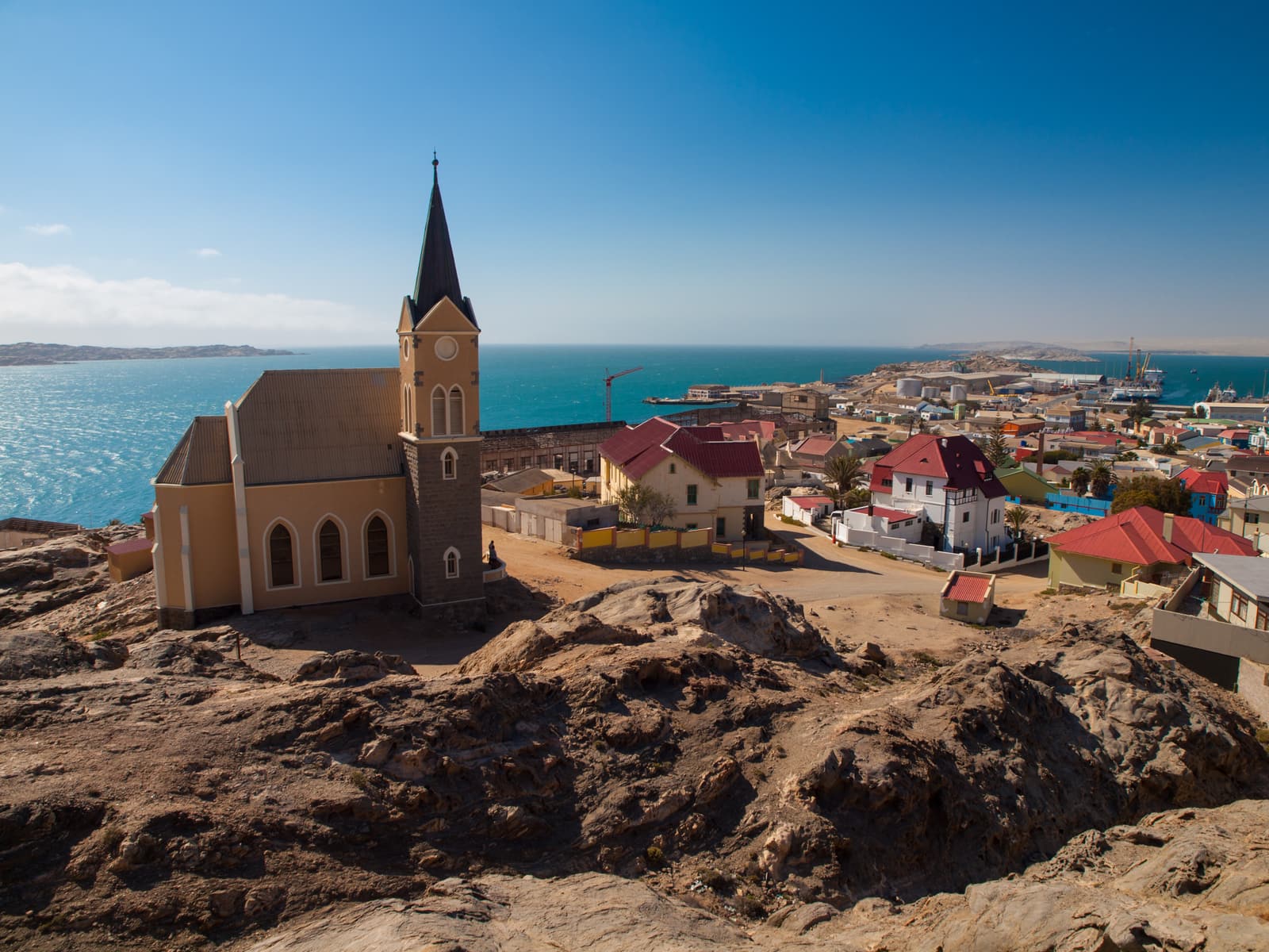 Die Felsenkirche auf einem Granitfelsen, dahinter rote Dächer und die Bucht von Lüderitz