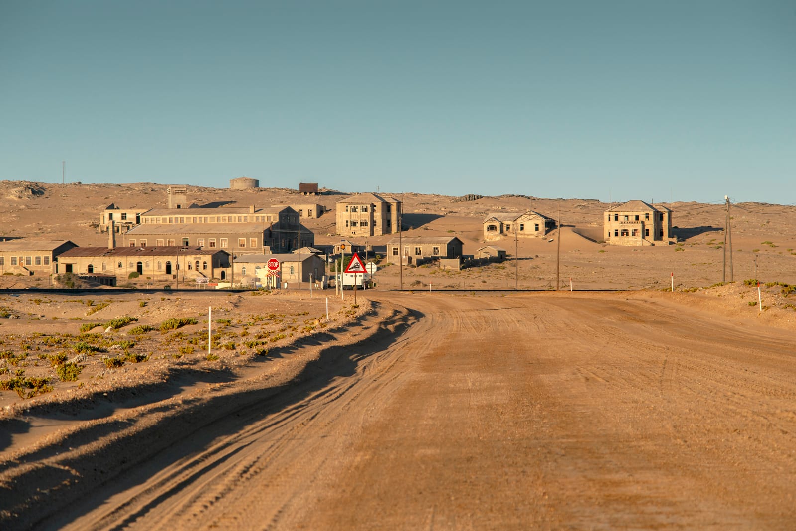 Sandpiste führt im Morgenlicht zu den Häusern der Geisterstadt Kolmanskop am Hang