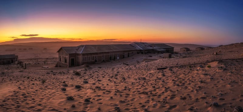 Lange Gebäudezeile als Silhouette im Sand bei Sonnenuntergang